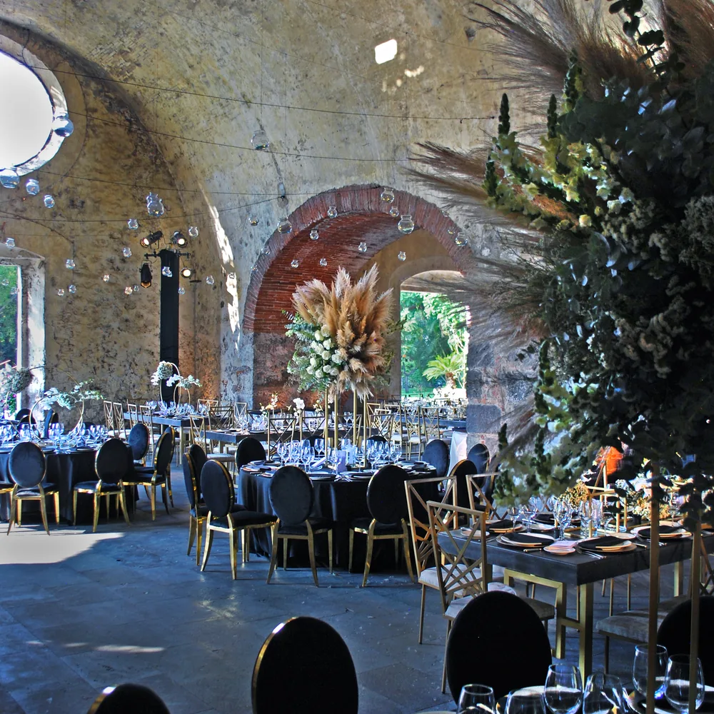 Banquete de AP Eventos en tonos negro y oro entre los muros de ladrillo de una hacienda, con mesas redondas y sillas de respaldo ovalado
