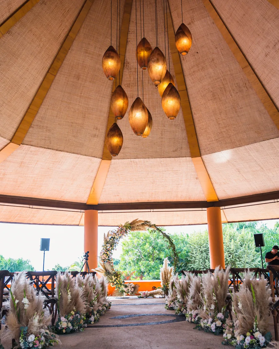 Ceremonia de boda al aire libre de AP Eventos con sillas cross-back de madera y arco circular de pampa