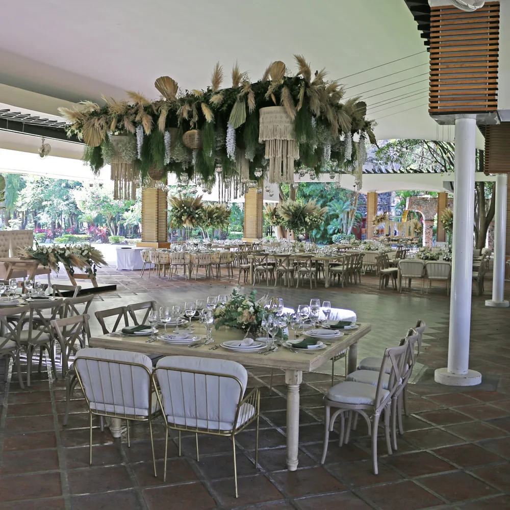 Salón montado por AP Eventos con instalación de pampas colgante sobre mesas largas y sillas cross-back