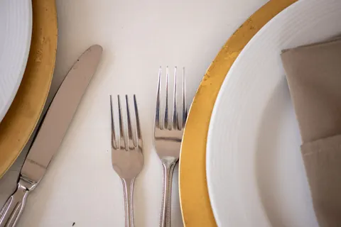 Detalle de cubiertos sobre mantel claro entre dos platos con borde dorado