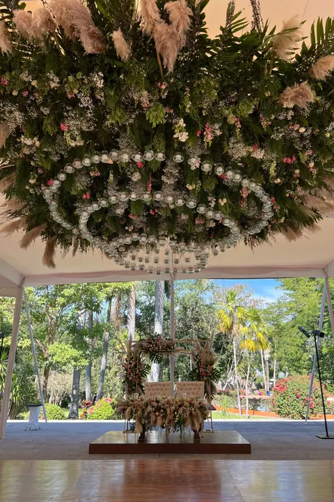 Instalación floral colgante con esferas de cristal sobre una pista y una mesa de novios al fondo