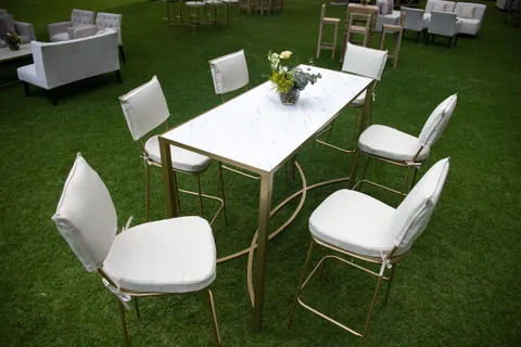 Mesa rectangular de mármol con base dorada y sillas tapizadas blancas sobre pasto