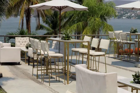 Periqueras doradas con bancos altos blancos en una terraza frente a un lago